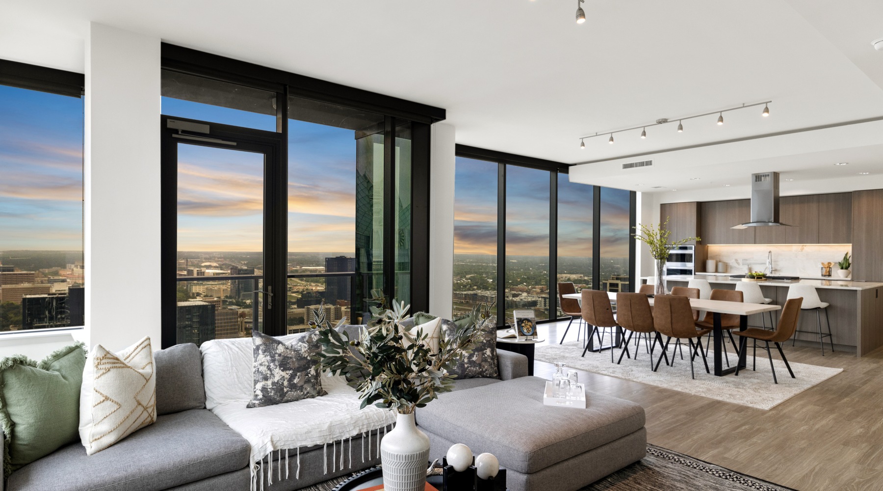 high-rise apartment with floor to ceiling windows, sectional sofa, 8-person dining table, and kitchen with island and vent hood